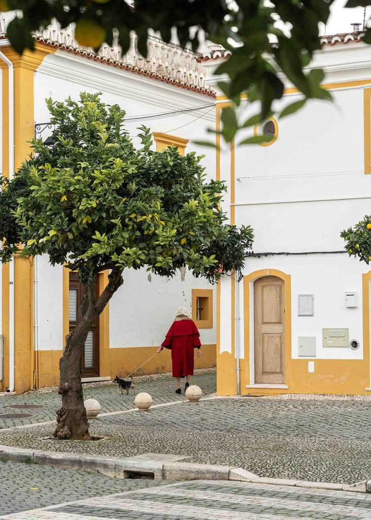 Lady wearing a capote, a traditional Alentejo coat, and walking her small dog in Vila Viscoça.