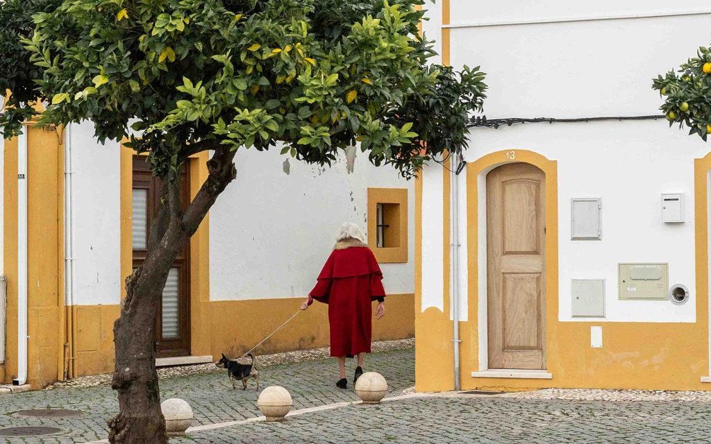 Lady wearing a capote, a traditional Alentejo coat, and walking her small dog in Vila Viscoça.